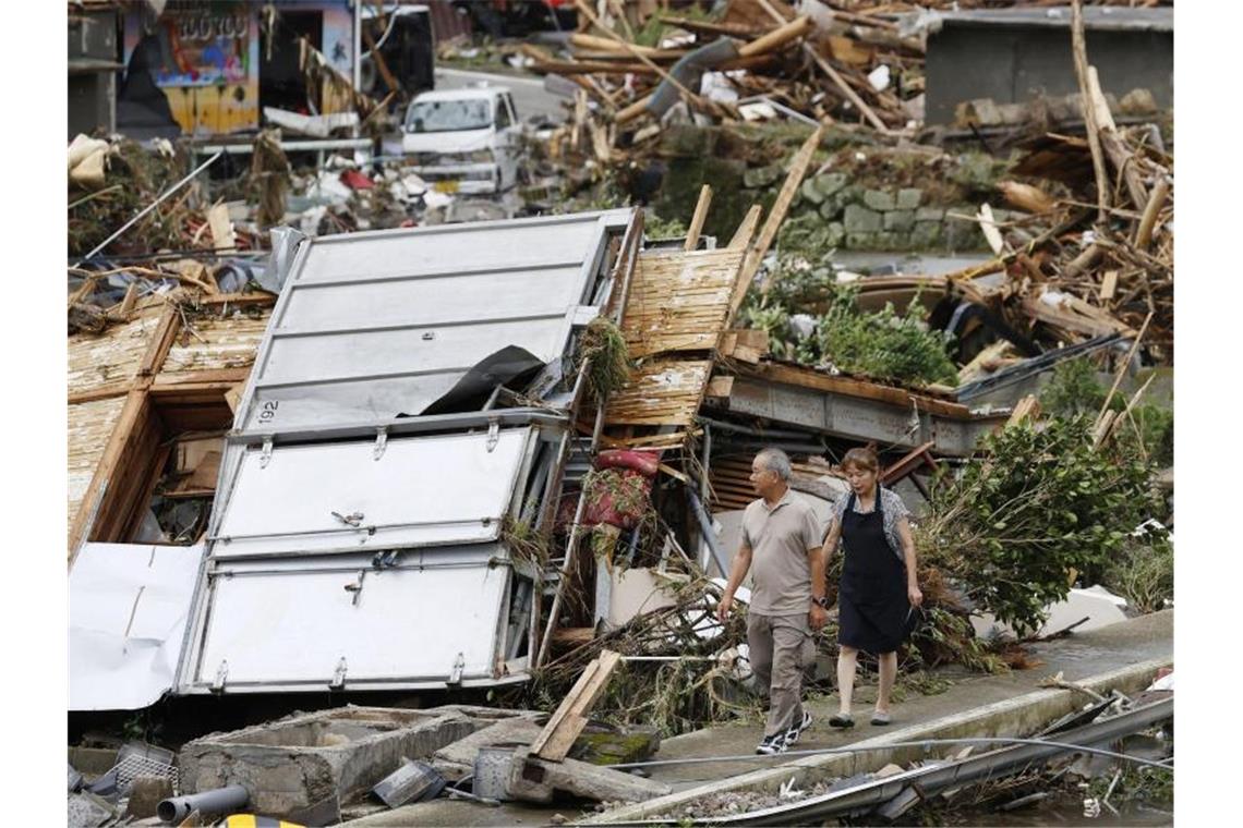 Ein Paar geht durch ein Trümmerfeld. Die Zahl der Todesopfer in den von schweren Unwettern heimgesuchten Überschwemmungsgebieten im Südwesten Japans ist weiter gestiegen. Foto: -/Kyodo News/AP/dpa