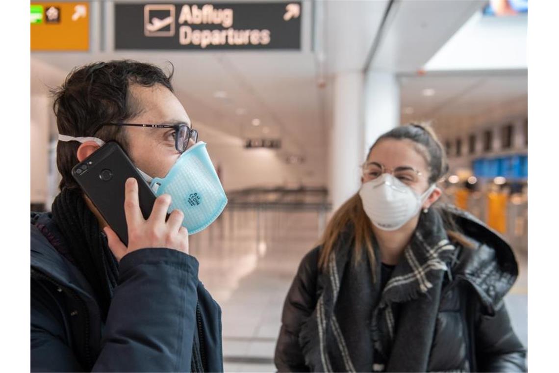 Ein Paar mit Mundschutz wartet auf dem Flughafen München auf den Flug in die Heimat - ins italienische Verona. Foto: Peter Kneffel/dpa