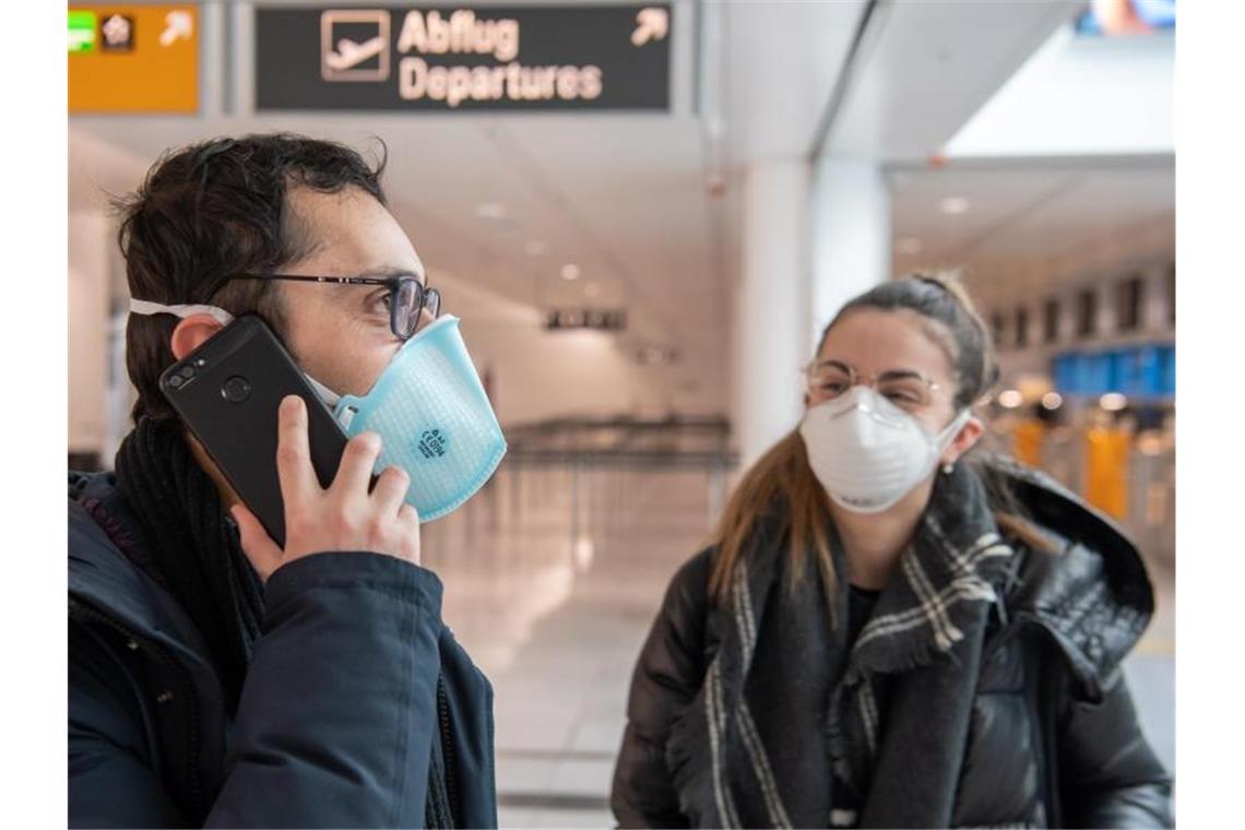 Megastaus an den Grenzen Ein Paar mit Mundschutz wartet auf dem Flughafen München auf den Flug in die Heimat - ins italienische Verona. Foto: Peter Kneffel/dpa