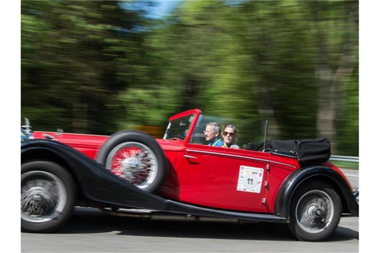 Ein Paar sitzt in eine Oldtimer und fährt über die Straße. Foto: Boris Roessler/Archivbild