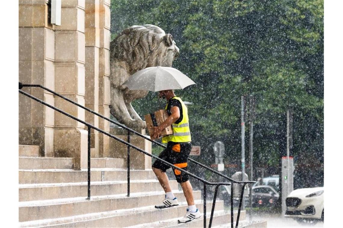 Ein Paketbote bringt im Platzregen seine Lieferungen ins Neue Rathaus von Hannover. Foto: Julian Stratenschulte/dpa