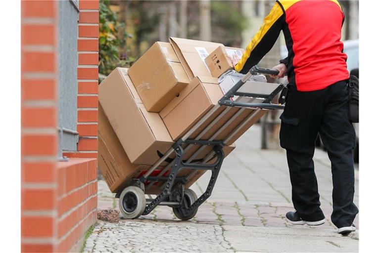 Ein Paketzusteller geht mit einer Sackkarre voller Pakete zu einem Haus. Foto: Jan Woitas/zb/dpa
