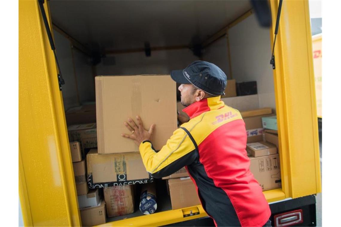 Ein Paketzusteller stellt ein Paket in ein Fahrzeug der Deutschen Post DHL. Foto: Rolf Vennenbernd/dpa