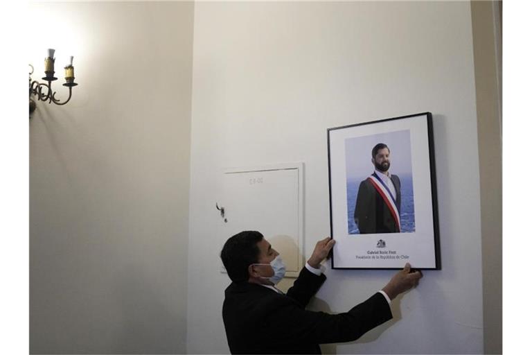 Ein Palastangestellter hängt das offizielle Porträt des neuen chilenischen Präsidenten Boric im Büro des Präsidentenpalastes La Moneda auf. Foto: Matias Delacroix/AP/dpa
