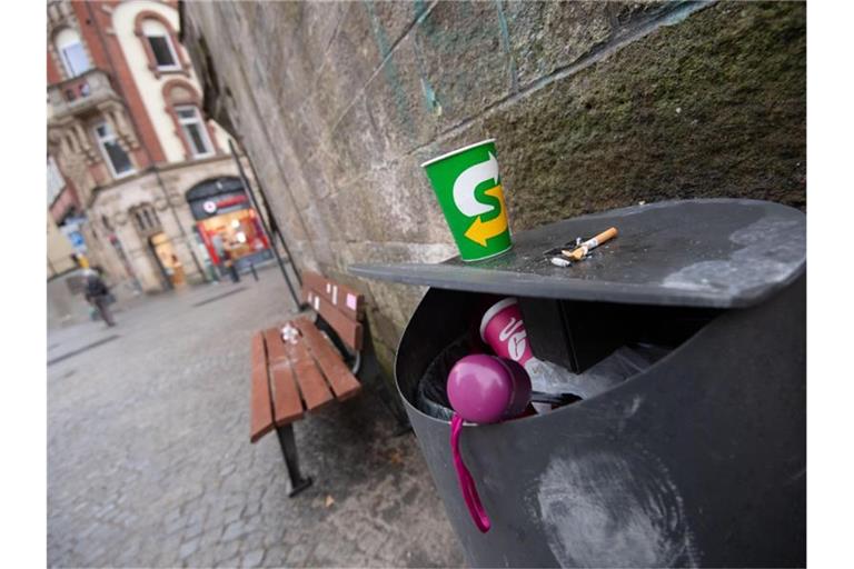 Ein Pappbecher und Zigarettenstummel liegen auf einem Mülleimer. Foto: Marijan Murat/dpa