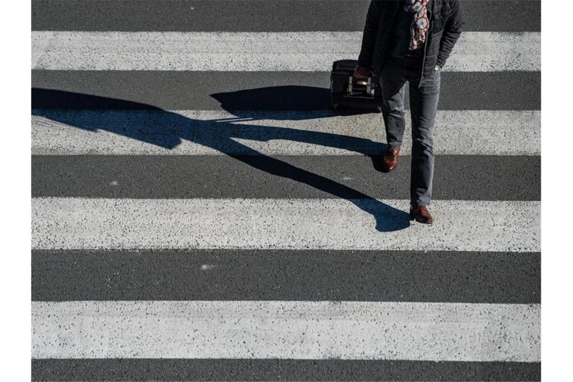 Ein Passagier geht mit seinem Rollkoffer über einen Zebrastreifen. Foto: Guido Kirchner/dpa/Archivbild