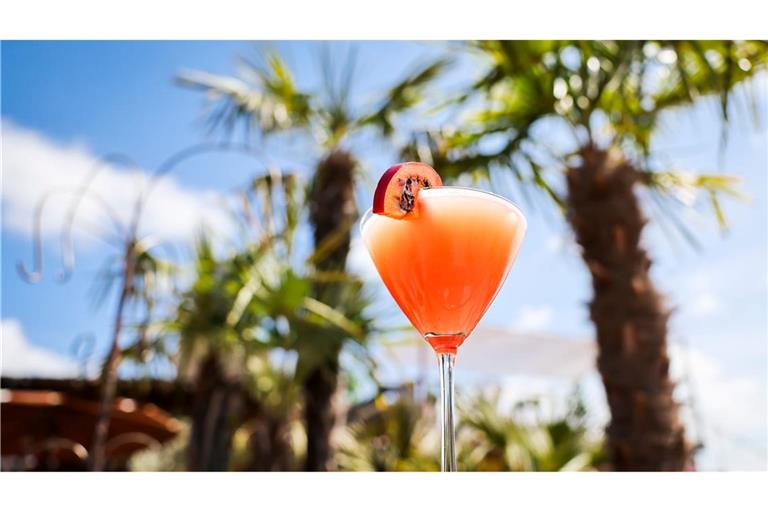 Ein Passionsfrucht Martini (auch Pornstar Martini oder Maverick Martini genannt) steht unter Palmen auf einem Tisch in einer Strandbar.