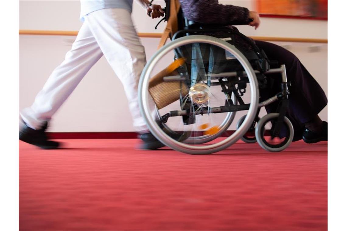 Ein Pfleger eines Pflegeheims schiebt eine Bewohnerin mit einem Rollstuhl. Foto: Tom Weller/dpa/Archiv