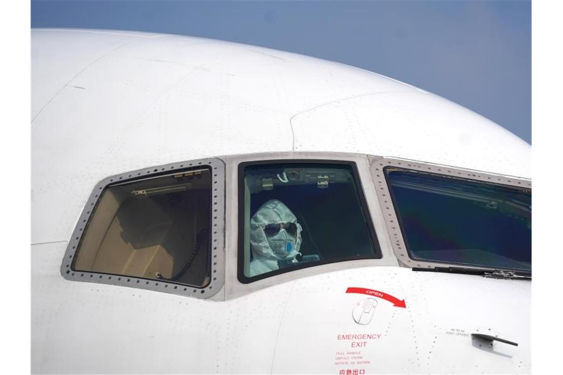 Ein Pilot sitzt mit Schutzanzug und Maske im Cockpit und parkt ein Flugzeug auf dem Internationalen Flughafen Wuhan-Tianhe. Foto: Cheng Min/XinHua/dpa
