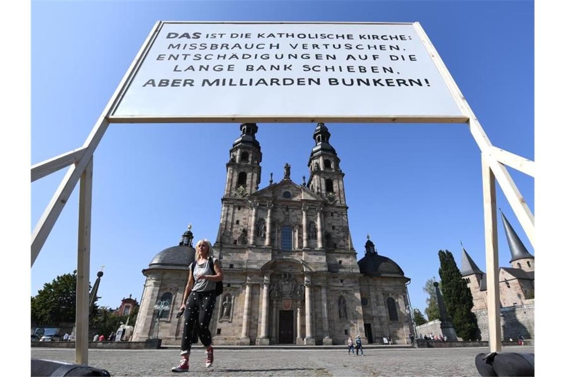 Ein Plakat der Giordano-Bruno-Stiftung mit der Aufschrift "DAS ist die Katholische Kirche: Missbrauch vertuschen. Entschädigungen auf die lange Bank schieben. Aber Milliarden bunkern !" steht am Rande der Herbstvollversammlung der Deutschen Bischofskonferenz auf dem Platz vor dem Dom. Foto: Arne Dedert/dpa