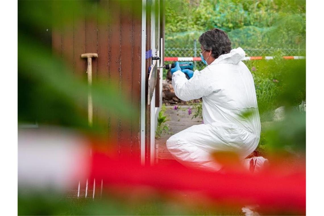 Ein Polizeibeamter der Spurensicherung kniet in der Kleingartenkolonie vor der Laube des vermutlichen Haupttäters. Foto: Guido Kirchner/dpa