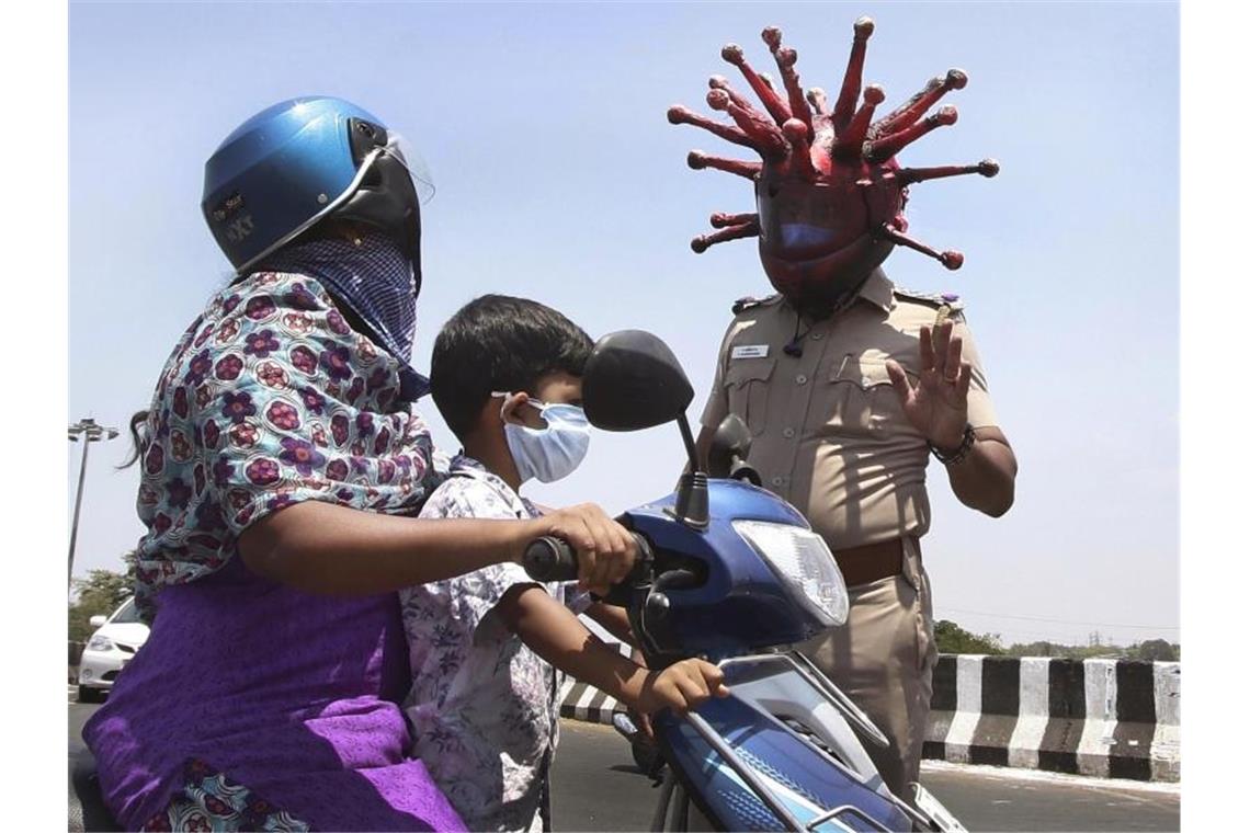 Corona global: Wie ein Virus die Welt verändert Ein Polizeibeamter im indischen Chennai trägt einen Helm, der einem Virus ähnelt, und weist Pendler auf die Einhaltung der Ausgangsbeschränkungen hin. Foto: R. Parthibhan/STR/AP/dpa