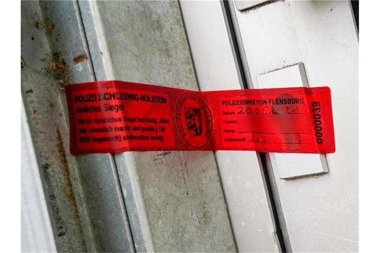 Ein Polizeisiegel klebt an einem Hauseingang in Kiel. In dem Haus wurde nach den Todesschüssen von Dänischenhagen eine dritte Leiche gefunden. Foto: Axel Heimken/dpa