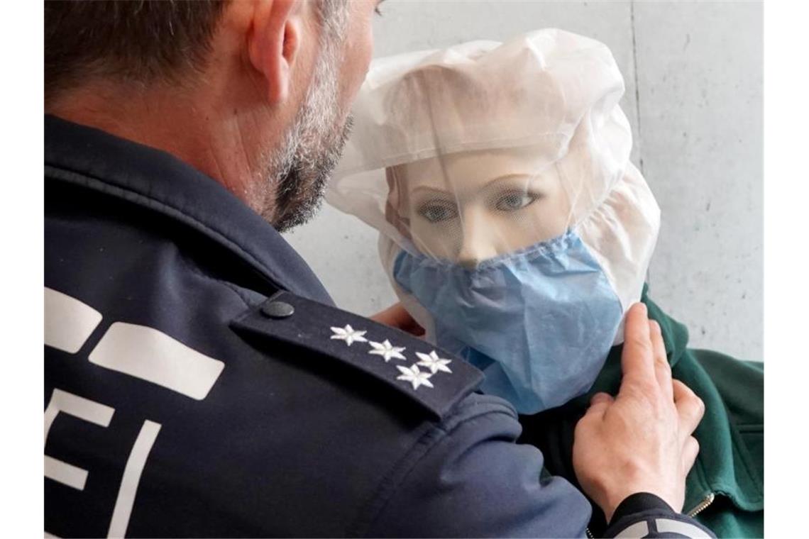 Ein Polizist demonstriert die Anwendung einer Spuckschutzhaube an einer Puppe. Foto: Simon Sachseder/dpa