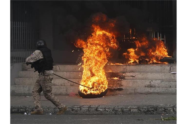 Ein Polizist entfernt einen brennenden Reifen vor einem Regierungsgebäude. Bei den Protesten gegen Haitis Regierung ist es in der Hauptstadt Port-au-Prince zu schweren Krawallen gekommen. Foto: Dieu Nalio Chery/AP