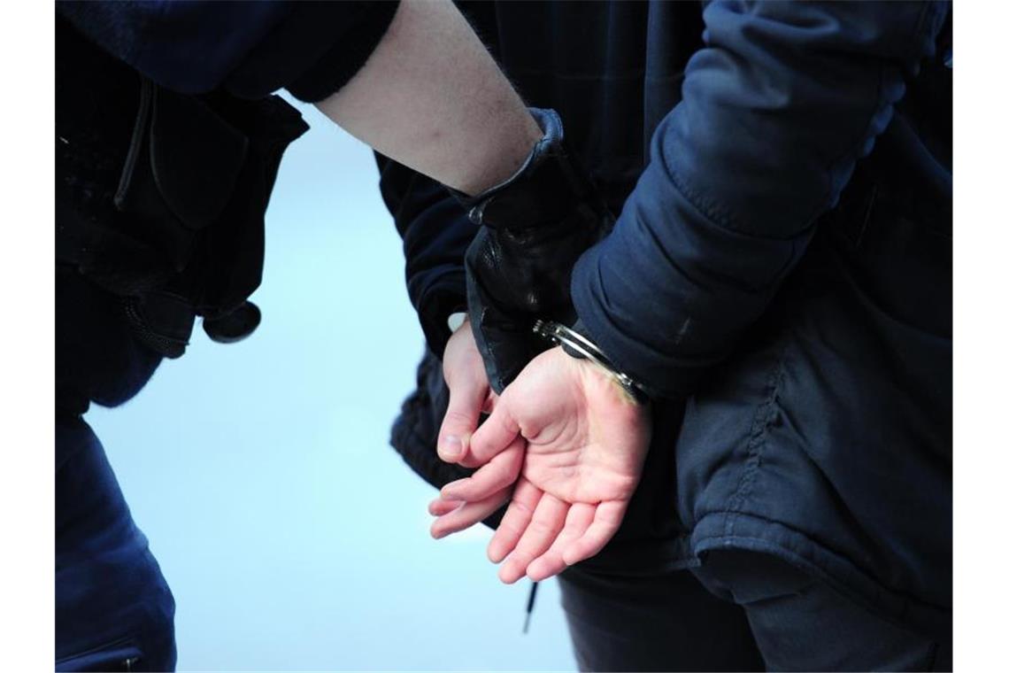 Fackel auf Roma-Familie geworfen: Haftbefehle erlassen Ein Polizist führt einen mit Handschellen gefesselten Mann ab. Foto: Daniel Reinhardt/Archivbild