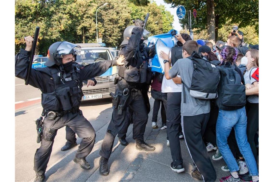 Ein Polizist hebt vor einer Gruppe von Demonstranten seinen Schlagstock. Foto: Peter Kneffel/dpa