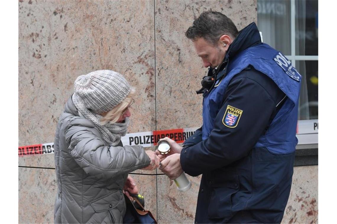 Ein Polizist hilft einer älteren Frau in der Nähe eines Tatortes am Heumarkt, eine Kerze anzuzünden. Foto: Boris Roessler/dpa