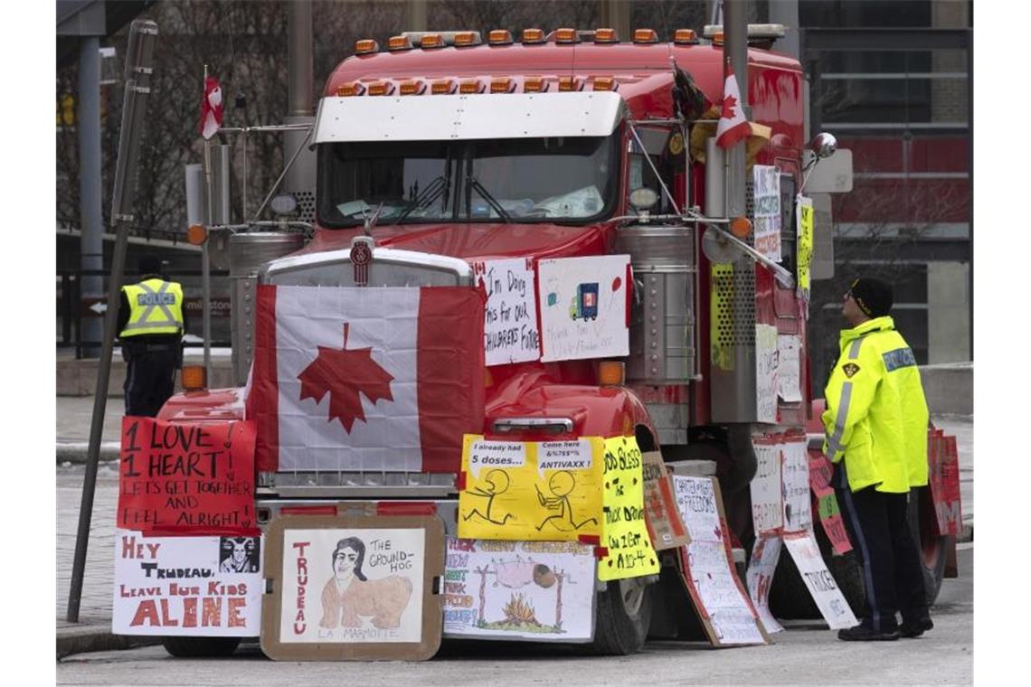 Ein Polizist in Ottawa im Gespräch mit einem Lastwagenfahrer, der sein Gefährt mit Schildern und Flaggen bedeckt hat. Foto: Adrian Wyld/The Canadian Press/AP/dpa