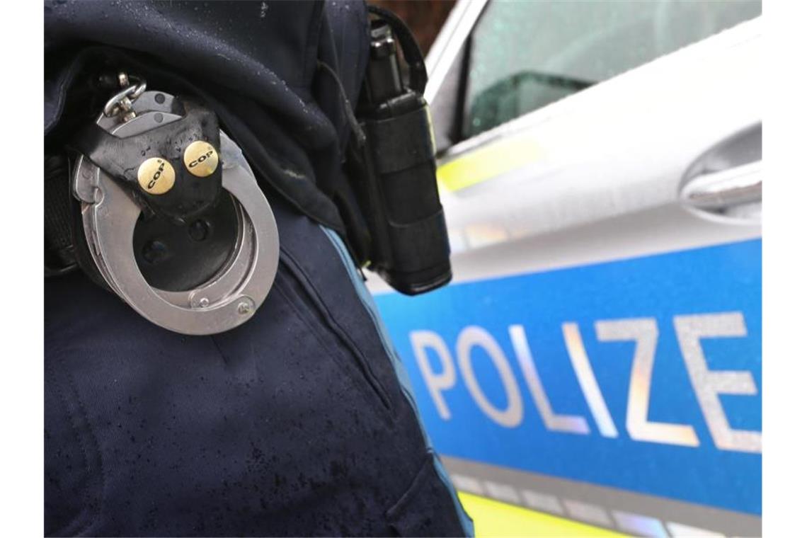 Ein Polizist mit Handschellen und einer Pistole am Gürtel steht vor einem Streifenwagen. Foto: Karl-Josef Hildenbrand/dpa