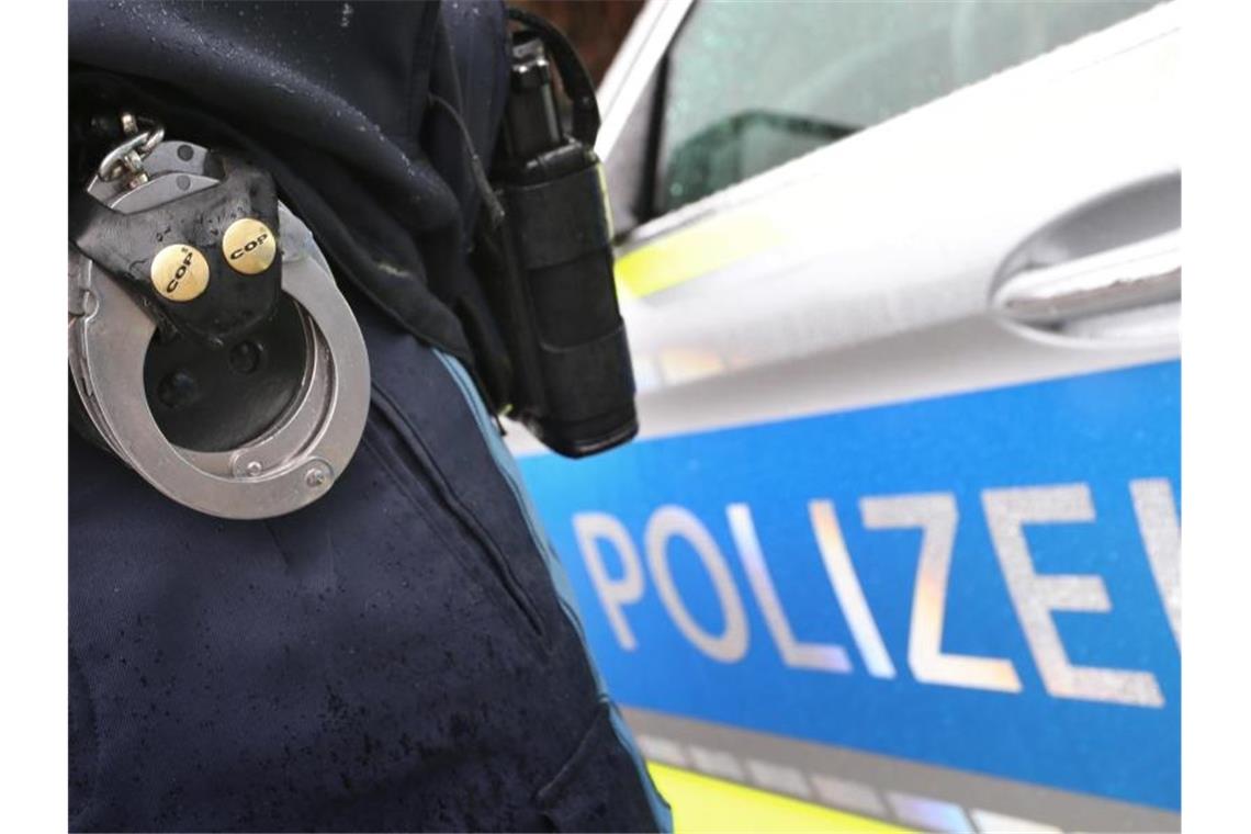 Ein Polizist mit Handschellen und einer Pistole am Gürtel steht vor einem Streifenwagen. Foto: Karl-Josef Hildenbrand/dpa/Symbolbild