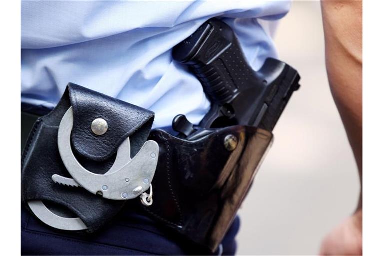 Ein Polizist mit Handschellen und Pistole am Gürtel steht auf einer Straße. Foto: Oliver Berg/dpa/Archivbild
