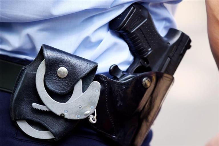 Ein Polizist mit Handschellen und Pistole am Gürtel steht am Straßenrand. Foto: Oliver Berg/dpa/Archivbild
