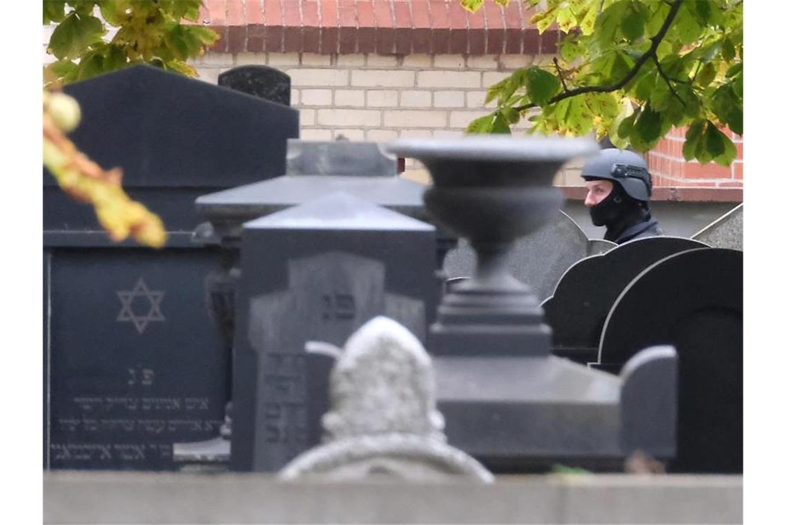 Ein Polizist mit Schutzhelm steht zwischen Grabsteinen auf dem jüdischen Friedhof von Halle. Foto: Sebastian Willnow/dpa-Zentralbild/dpa