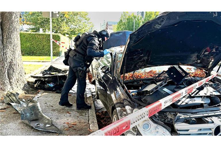 Ein Polizist mit Schutzweste steht an einem PKW, der gebrant hatte. Ein Brand in einem Münchner Einfamilienhaus hat einen Großeinsatz von Polizei und Feuerwehr ausgelöst.