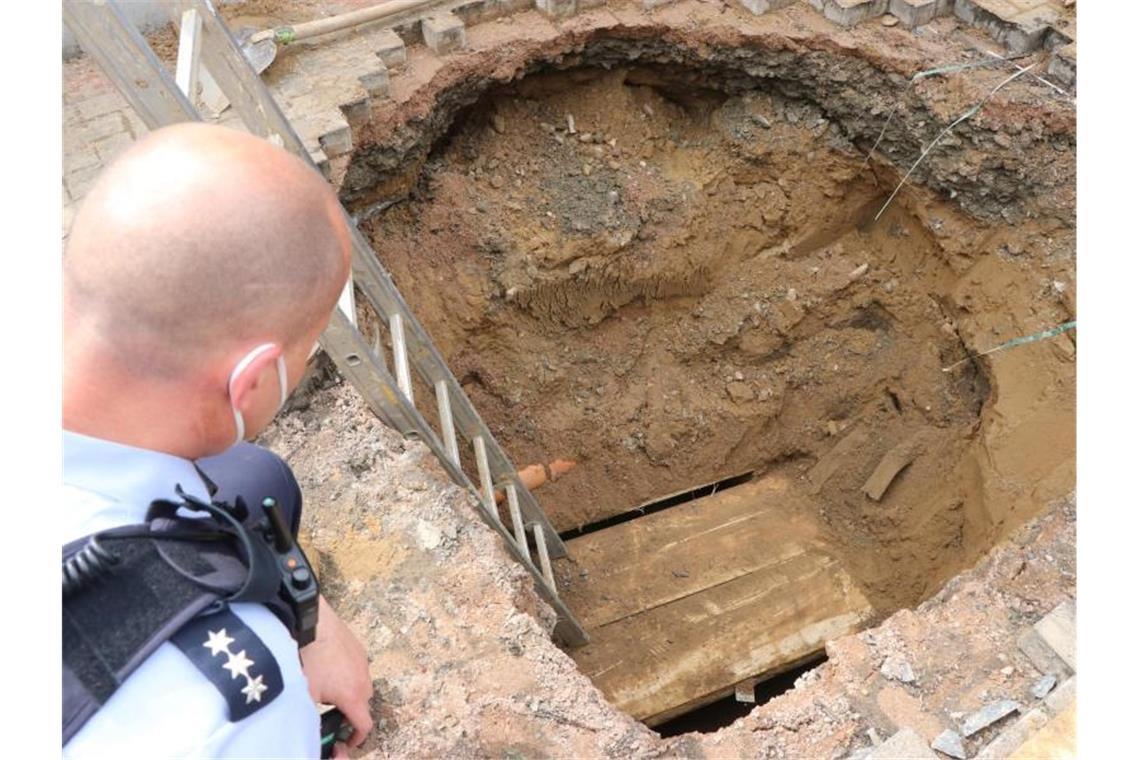 Ein Polizist schaut auf das Loch eines Tunnels, den Unbekannte zur Volksbank gegraben haben. Foto: Ekkehard Wind/dpa