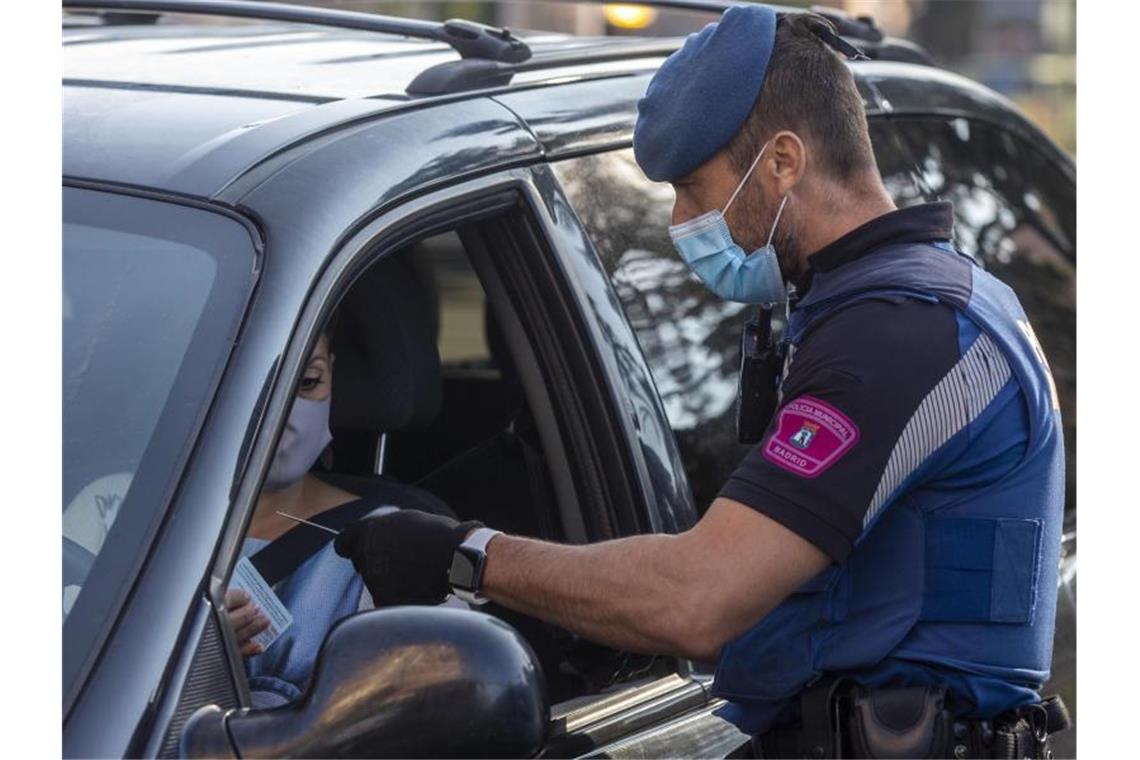 Tausende Tote, zweiter Lockdown: Corona-Hotspots weltweit Ein Polizist spricht an einem Kontrollpunkt in Madrid mit einer Autofahrerin. Foto: Manu Fernandez/AP/dpa