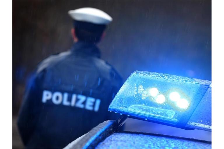 Ein Polizist steht im Regen vor einem Streifenwagen dessen Blaulicht aktiviert ist. Foto: Karl-Josef Hildenbrand/dpa/Illustration