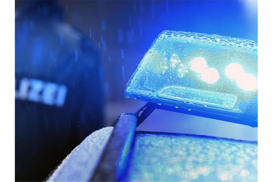 Ein Polizist steht im Regen vor einem Streifenwagen dessen Blaulicht aktiviert ist. Foto: Karl-Josef Hildenbrand/dpa/Archivbild
