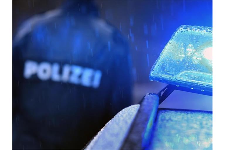 Ein Polizist steht im Regen vor einem Streifenwagen dessen Blaulicht aktiviert ist. Foto: Karl-Josef Hildenbrand/dpa/Symbolbild