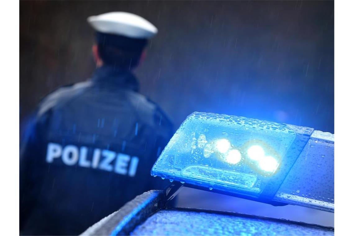 Ein Polizist steht im Regen vor einem Streifenwagen dessen Blaulicht aktiviert ist. Foto: Karl-Josef Hildenbrand/Archiv