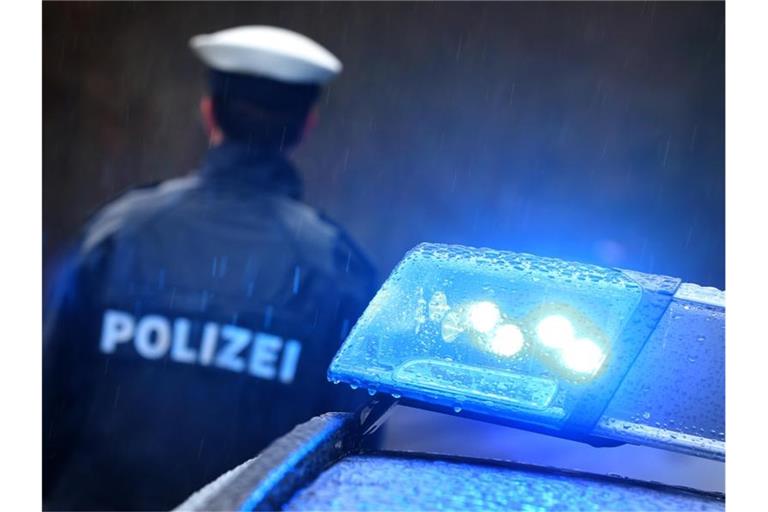 Ein Polizist steht im Regen vor einem Streifenwagen dessen Blaulicht aktiviert ist. Foto: Karl-Josef Hildenbrand/Archiv