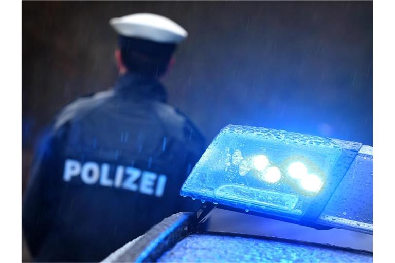 Ein Polizist steht im Regen vor einem Streifenwagen dessen Blaulicht aktiviert ist. Foto: Karl-Josef Hildenbrand/dpa/Archivbild