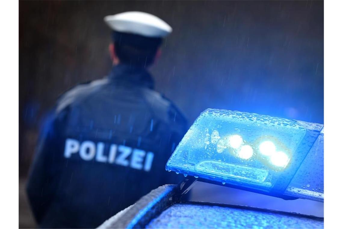 Ein Polizist steht im Regen vor einem Streifenwagen dessen Blaulicht aktiviert ist. Foto: Karl-Josef Hildenbrand/dpa/Illustration