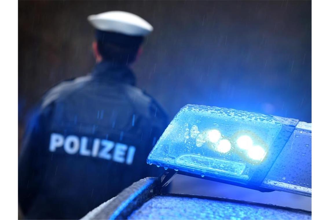 Ein Polizist steht im Regen vor einem Streifenwagen dessen Blaulicht aktiviert ist. Foto: Karl-Josef Hildenbrand/dpa/Archivbild