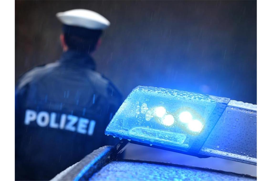 Ein Polizist steht im Regen vor einem Streifenwagen dessen Blaulicht aktiviert ist. Foto: Karl-Josef Hildenbrand/dpa/Archivbild