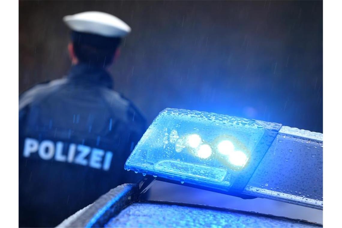 Ein Polizist steht im Regen vor einem Streifenwagen. Foto: Karl-Josef Hildenbrand/dpa/Archivbild