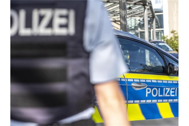 Ein Polizist steht vor einem Streifenwagen. Foto: David Inderlied/dpa/Illustration