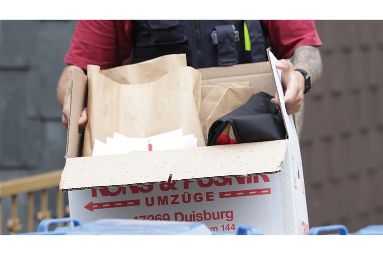 Ein Polizist trägt nach einer Wohnungsdurchsuchung einen Karton mit sichergestellten Gegenständen.