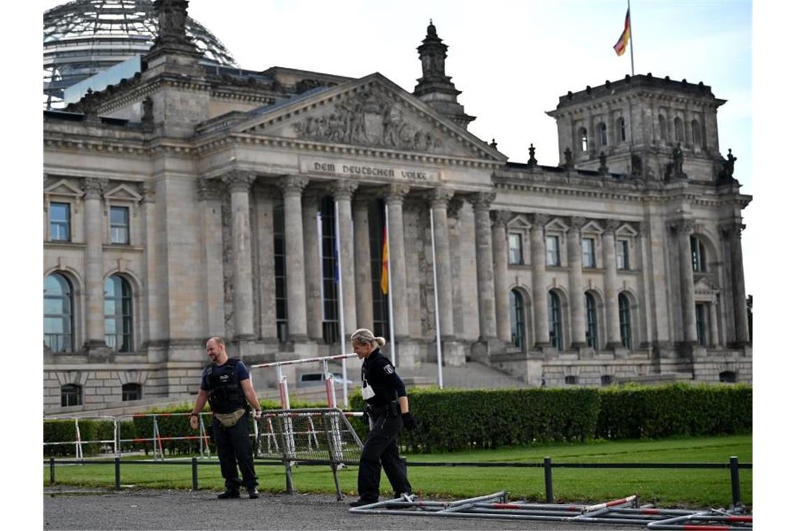 Ein Polizist und eine Polizistin tragen eine Absperrung am Reichstagsgebäude weg. Foto: Johannes Neudecker/dpa