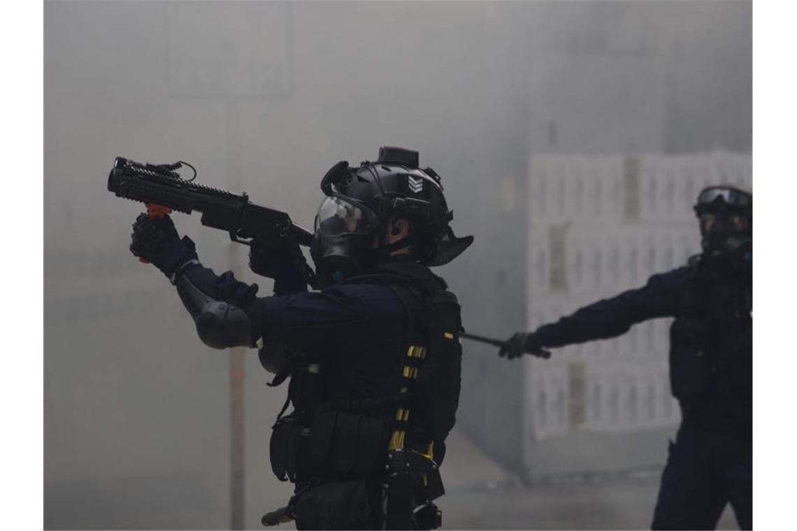 Ein Polizist zielt mit Tränengas auf Demonstranten bei regierungskritischen Protesten. Foto: Ng Han Guan/AP/dpa