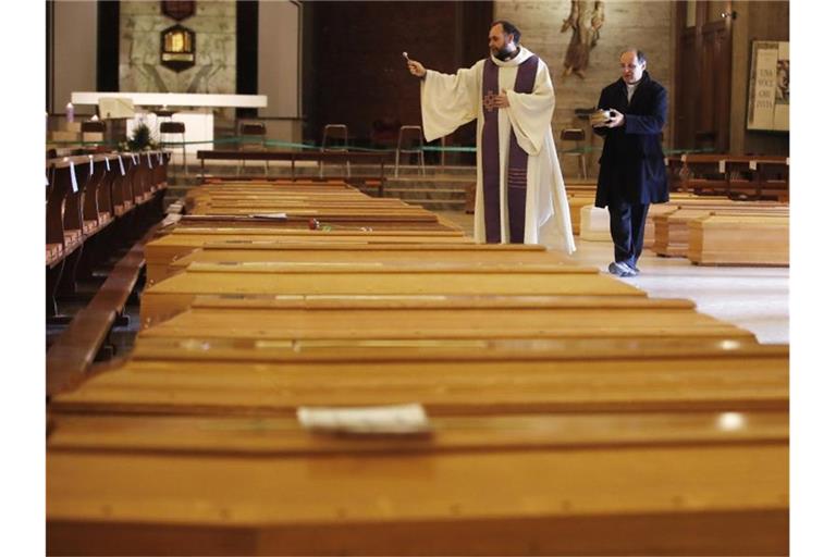 Ein Priester segnet Särge in Seriate, einer Gemeinde in der italienischen Provinz Bergamo. Foto: Antonio Calanni/AP/dpa