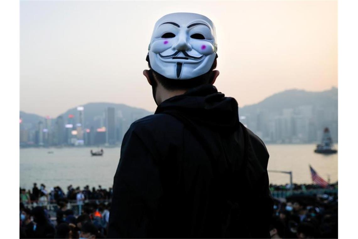 Hongkong: Neue Proteste, neue Ausschreitungen Ein prodemokratischer Demonstrant mit Guy-Fawkes-Maske beobachtet eine Kundgebung in Hongkong. Foto: Vincent Thian/AP/dpa