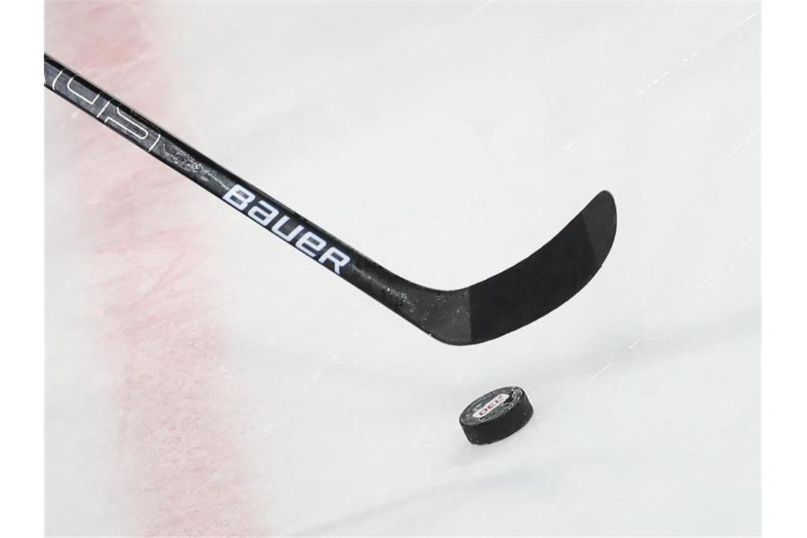 Ein Puck liegt vor einem Eishockey-Schläger auf dem Eis. Foto: Daniel Karmann/dpa/Symbolbild