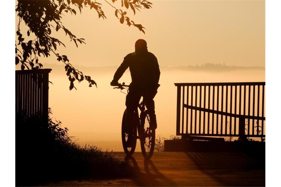 Ein Radfahrer fährt bei Sonnenaufgang über eine Brücke. Foto: Thomas Warnack/dpa/Symbolbild