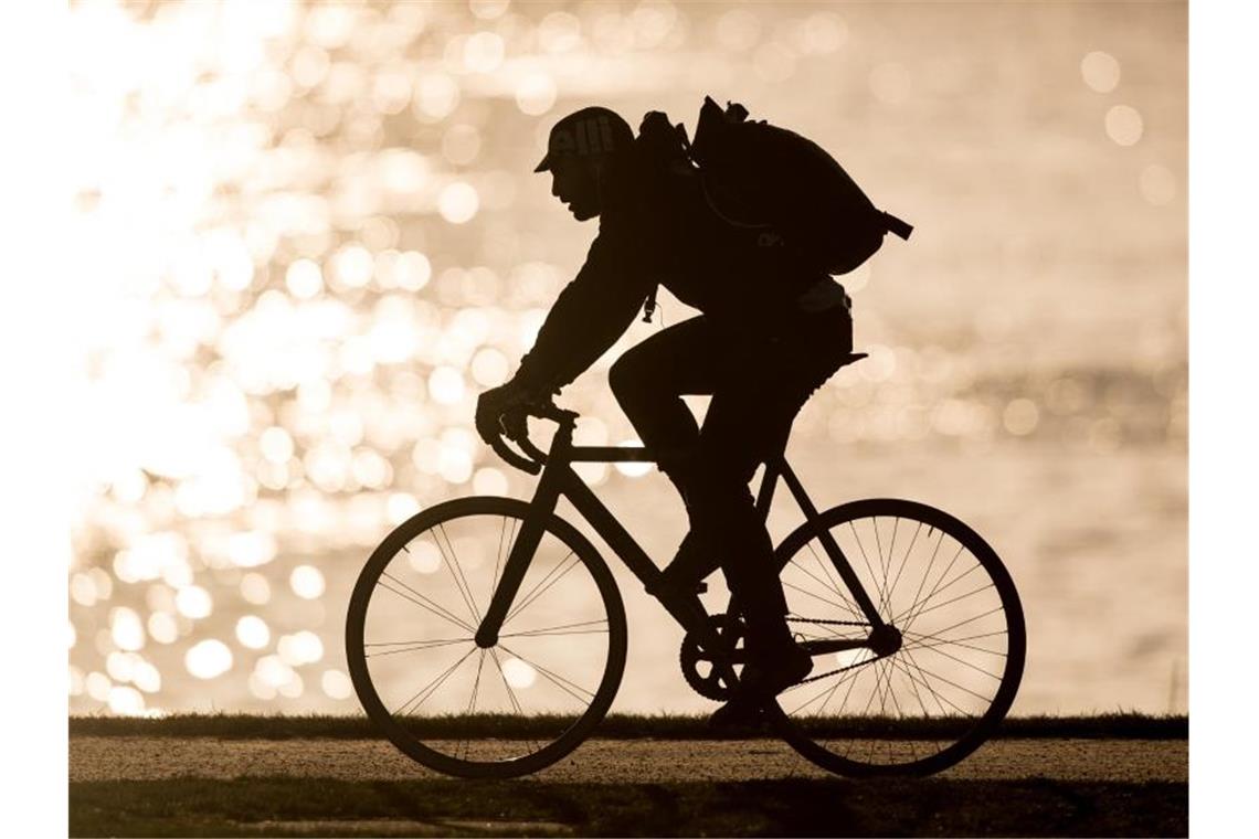 Ein Radfahrer fährt im Gegenlicht an einem Fluss entlang. Foto: Fabian Sommer/Archivbild